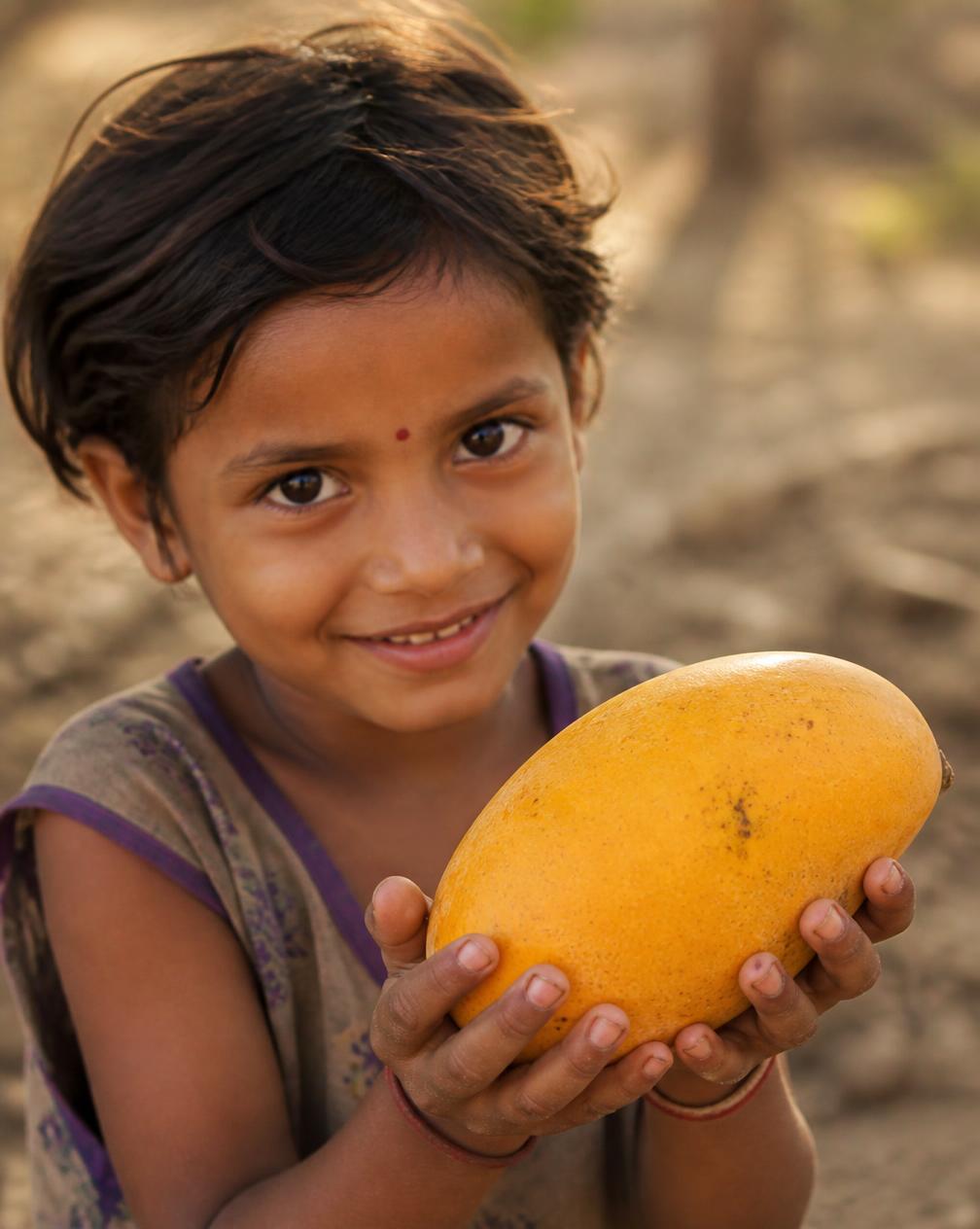 A child in rural Gujarat smiling while holding a fresh ripe mango